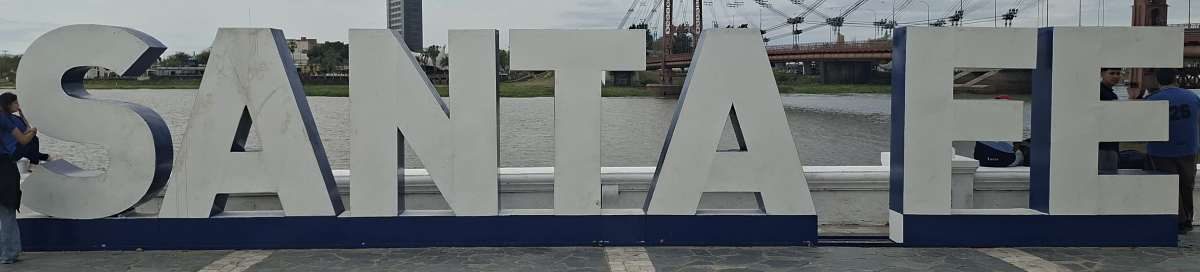 The city name sign is at the waterfront near the suspension bridge.